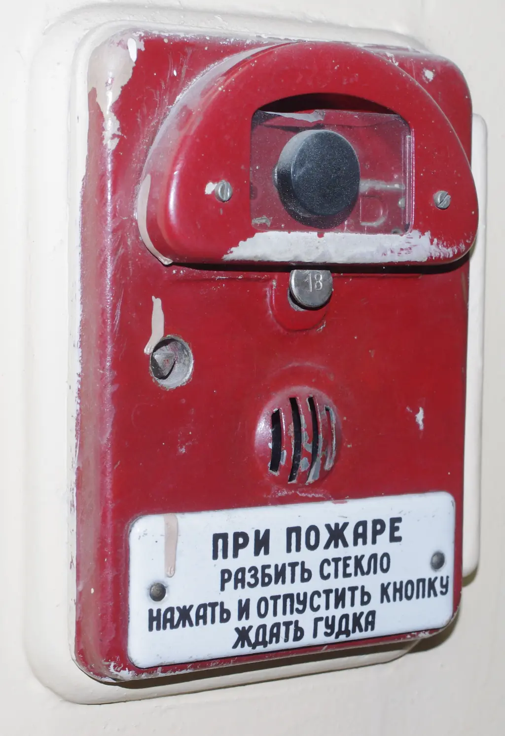 Ручной пожарный извещатель старого образца в МГУ, снимок 2014 года: кнопка под стеклом, а на эмалевой табличке — своя короткая инструкция «При пожаре разбить стекло, нажать и отпустить кнопку, ждать гудка». Фото: Artyom Svetlov, CC BY 4.0