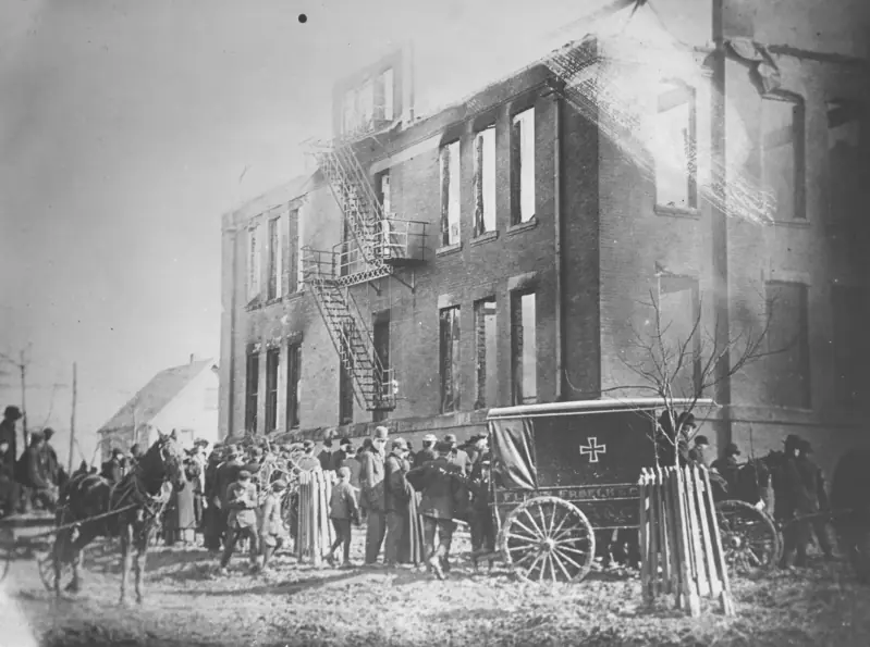 Руины школы Лейк-Вью после пожара 4 марта 1908 года: выгоревшие окна, наружные пожарные лестницы на фасаде, толпа и санитарный фургон у здания. Источник: Cleveland Public Library, общественное достояние